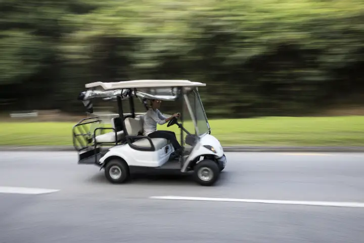 Golf cart driving fast along a paved road