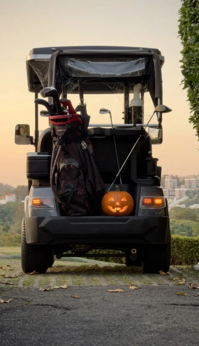 Golf cart at dusk with a bag of clubs and a lit jack-o'-lantern on the back